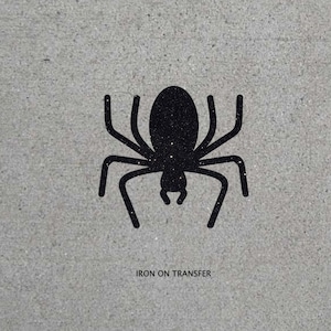 May include: Black iron-on transfer of a spider silhouette. The spider has a glittery finish. The text "IRON ON TRANSFER" is printed below the spider.