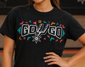May include: Black t-shirt with the text "GO GO" in white and teal, featuring a star and lightning bolt design. The shirt has colorful geometric patterns above the text. The shirt is short-sleeved.