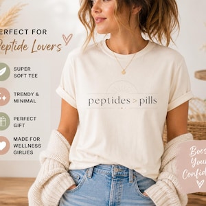 May include: Cream-colored t-shirt with the text "peptides > pills" in a minimalist font. The shirt is paired with blue jeans. Additional text includes "Super Soft Tee," "Trendy & Minimal," and "Perfect Gift."