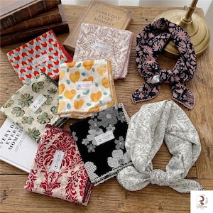 May include: A collection of square fabric scarves and handkerchiefs featuring various patterns including red and blue chevrons, yellow hearts, green leaves, black and white floral prints, and red damask, each with a small white brand label.