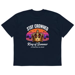 Könnte beinhalten: Marineblaues T-Shirt mit einer Grafik einer goldenen Krone, Palmen und den Worten "Stay Crowned" und "King of Summer". Das Design beinhaltet einen Sonnenuntergangshintergrund und den Satz "Live Bold Rule Your World".