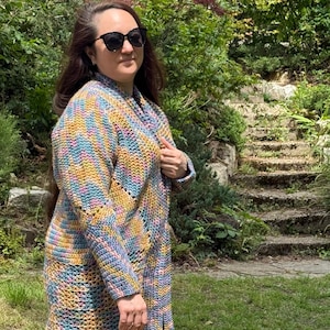 Peut inclure: Un cardigan long à manches longues arrivant au genou, doté d'un motif en maille crochetée texturée. Le vêtement est réalisé en fil multicolore mélangeant des tons bleu, jaune, rose et orange, avec un col châle et une ouverture frontale.