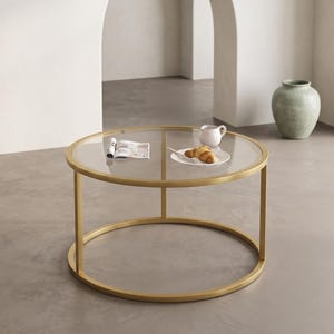 May include: A round coffee table featuring a clear glass top and a gold-toned metal frame. The table has a circular base and vertical supports connecting the top rim to the bottom ring, creating an open, airy structure for the living space.