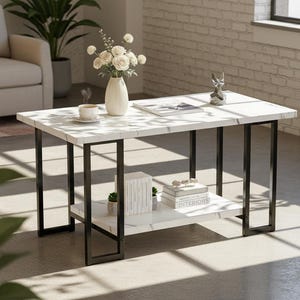 May include: A rectangular coffee table with a white marble-look top and a black metal frame. The table has a lower shelf for storage. A vase of white flowers, books, and decorative items are on the table.