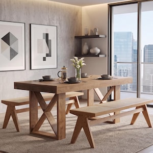 May include: A rectangular wooden dining table with a cross-leg base and two matching benches featuring woven cane seats. The table is set with dark gray bowls, a glass French press, and a clear glass vase containing white calla lilies.