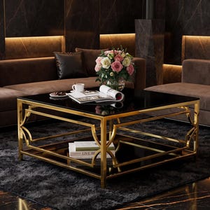 May include: A square coffee table featuring a polished gold metal frame with geometric side detailing and two black glass surfaces. The top surface holds a glass vase with pink and white roses, a white ceramic cup, and an open magazine.