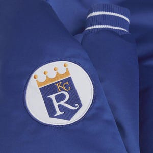 May include: Royal blue satin jacket with a white and gold embroidered patch featuring a crown, the letters "KC", and the letter "R". The jacket has a ribbed collar and cuffs with white stripes.
