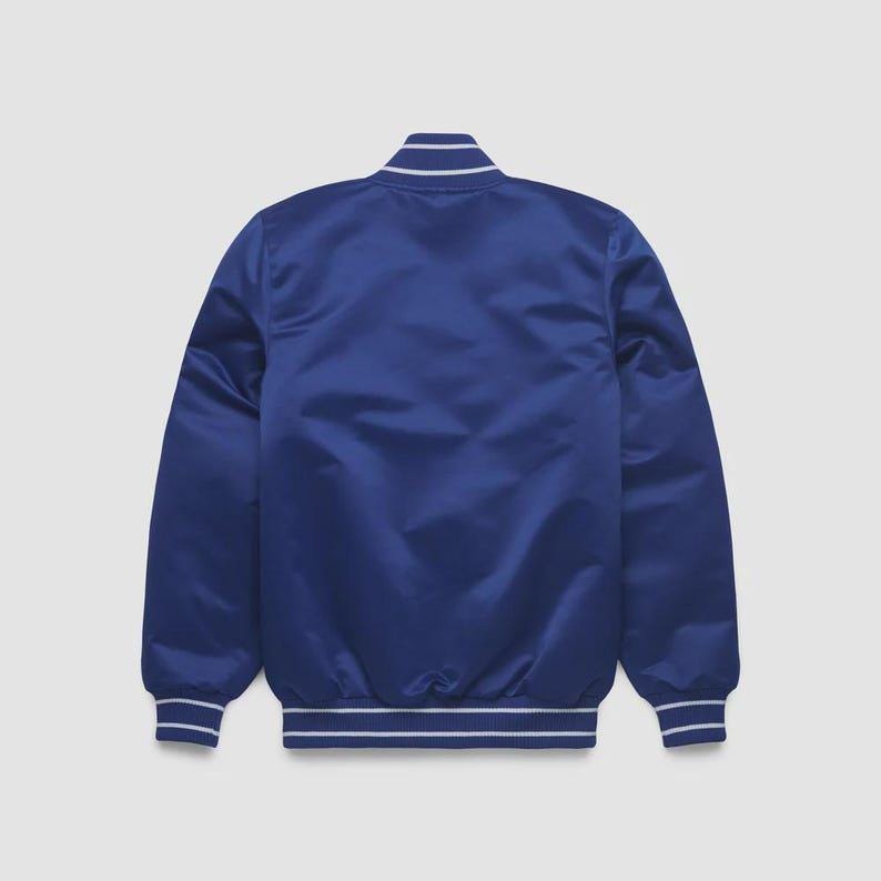 May include: A royal blue satin bomber jacket with white striped trim on the collar, cuffs, and hem. The back of the jacket is smooth and unadorned, with a slight sheen. The jacket is a classic style.