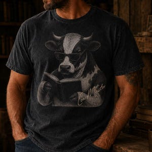 Puede incluir: Camiseta gris oscuro con una ilustración en blanco y negro de una vaca con gafas de sol leyendo un libro. El texto "Con Master" está escrito debajo. La camiseta la lleva una persona.