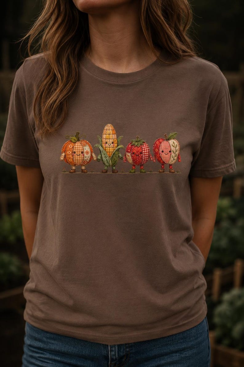 K&ouml;nnte beinhalten: Ein braunes Kurzarm-T-Shirt mit einem Grafikdruck von vier anthropomorphen Obst- und Gem&uuml;sesorten, darunter ein K&uuml;rbis, ein Maiskolben, eine Tomate und ein Apfel, die alle mit einem Patchwork-Muster und l&auml;chelnden Gesichtern gestaltet sind.