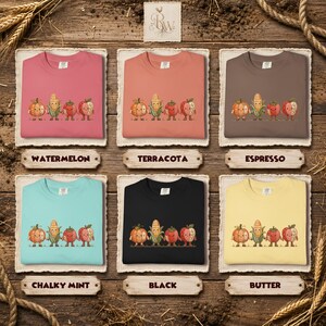 K&ouml;nnte beinhalten: Sechs Rundhals-Sweatshirts in den Farben Wassermelone, Terrakotta, Espresso, Kreideminze, Schwarz und Butter. Jedes Shirt zeigt eine Grafik von vier handhaltenden Cartoon-Gem&uuml;sesorten, darunter ein K&uuml;rbis, ein Maiskolben, eine Erdbeere und ein Apfel.
