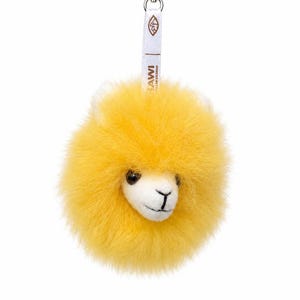 Op de afbeelding: Een gele alpaca sleutelhanger met een wit gezicht en een pluizig, rond lichaam. De sleutelhanger heeft een zilveren sluiting en een witte band met bruine tekst "LAWI COLLECTION".