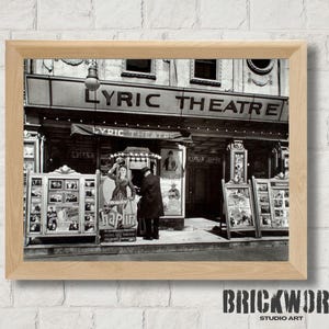 Könnte beinhalten: Gerahmter Schwarz-Weiß-Druck des Lyric Theatre. Das Schild über dem Eingang lautet "LYRIC THEATRE". Plakate und Werbung sind an den Seiten ausgestellt. Ein Mann und eine Frau stehen vor dem Theater.