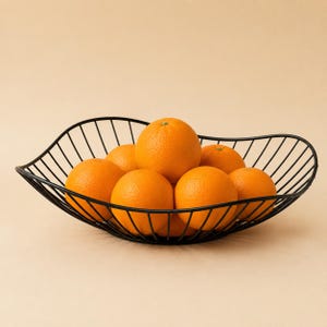 May include: A black wire fruit bowl with a wavy, open-frame design holding seven bright orange citrus fruits. The bowl features a curved, elongated shape constructed from thin metal rods, providing a clear view of the round oranges inside.