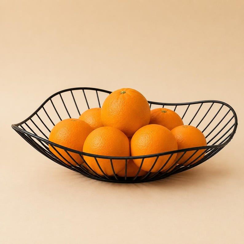 May include: A black wire fruit bowl with a wavy, open-frame design holding seven bright orange citrus fruits. The bowl features a curved, elongated shape constructed from thin metal rods, providing a clear view of the round oranges inside.
