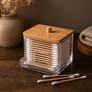 May include: A clear acrylic storage container with a bamboo lid and a small knob, filled with bamboo cotton swabs. The container features a front-facing rectangular cutout for dispensing individual swabs, with three additional cotton swabs lying nearby.
