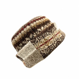 May include: A knitted cuff or wrist warmer featuring a complex Fair Isle pattern in shades of brown, beige, and cream, accented by thin horizontal stripes of deep red. The accessory has a textured, wool-like appearance with a ribbed edge.