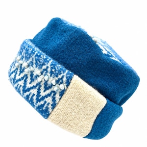 May include: A blue felted wool hat featuring a folded brim with a white and blue zigzag knit pattern. The brim is accented with small, light-colored beads along the zigzag design and includes a solid cream-colored knit section.