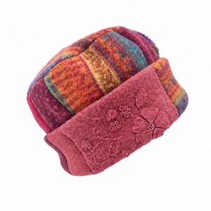 May include: A felted wool hat featuring a multi-colored plaid pattern in shades of orange, purple, and blue. The hat includes a solid dark pink band decorated with embroidered floral motifs and small beads across the front surface.