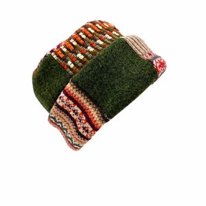 May include: A patchwork beanie constructed from various knit fabrics. The hat features panels of solid dark green felted wool, sections with a multi-colored orange and brown vertical stripe pattern, and a band with a detailed red and white geometric design.