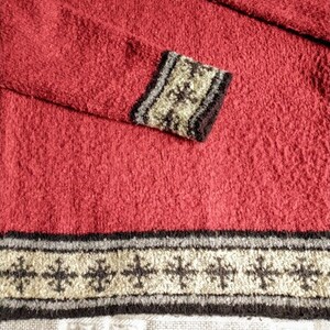 May include: A red textured sweater with decorative cuffs and hem. The cuffs and hem feature a repeating pattern in beige, black, and gray. The sweater has a crew neck and long sleeves.