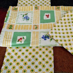 May include: Three fabric placemats with a yellow and green checkered pattern, a green and white floral pattern, and a white background with yellow daisy flowers.