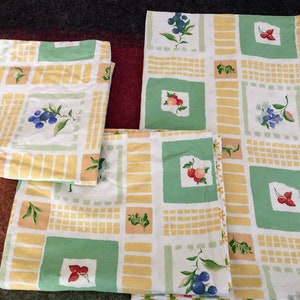 May include: Three fabric placemats with a yellow and green checkered pattern. The placemats feature a variety of fruit and floral designs, including blueberries, strawberries, and flowers.