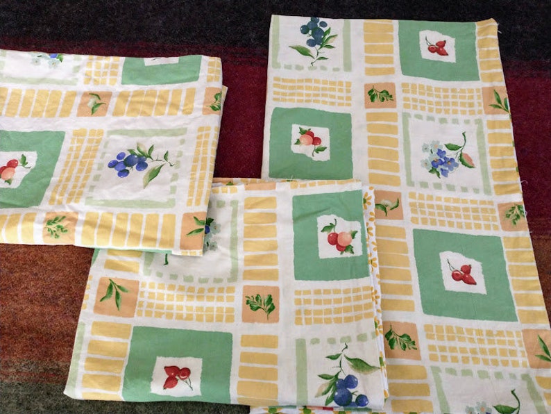 May include: Three fabric placemats with a yellow and green checkered pattern. The placemats feature a variety of fruit and floral designs, including blueberries, strawberries, and flowers.