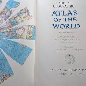 May include: The title page of the National Geographic Atlas of the World, Fourth Edition, 1975. The right side features blue text on a white background, while the left side displays a segmented, colorful map of the Arctic region in blue and white.