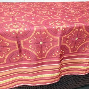 May include: A red tablecloth with a repeating geometric pattern in shades of orange and burgundy. The design features circular and floral motifs. The border has horizontal stripes in orange, burgundy, and yellow.