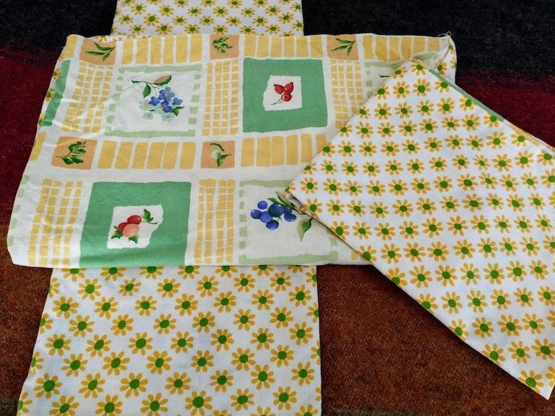 May include: Three fabric placemats with a yellow and green checkered pattern, a green and white floral pattern, and a white background with yellow daisy flowers.