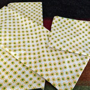 May include: A set of three white fabric pillowcases with a yellow and green daisy print.