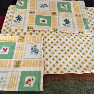 May include: Three yellow and green patterned fabric squares with a floral design. The fabric has a white background with yellow and green squares and a floral pattern in the center of each square. The fabric is folded in thirds.