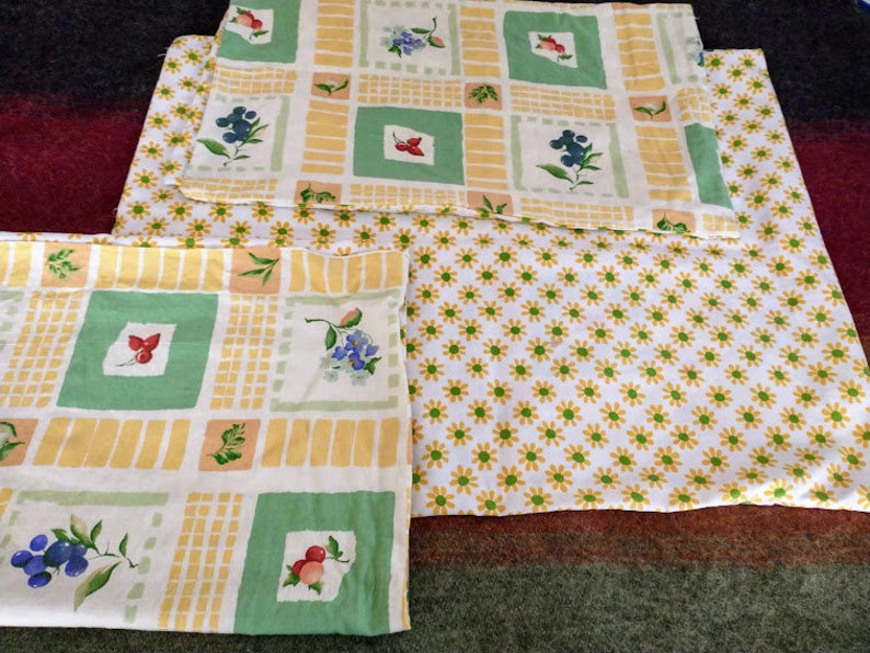 May include: Three yellow and green patterned fabric squares with a floral design. The fabric has a white background with yellow and green squares and a floral pattern in the center of each square. The fabric is folded in thirds.