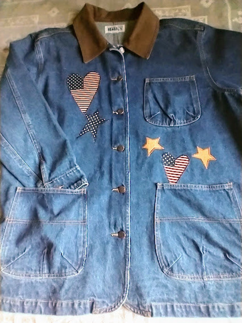 May include: A blue denim jacket with a brown corduroy collar. The jacket has a variety of patches, including hearts, stars, and a small American flag. The jacket has two large pockets on the front and a smaller pocket on the right side of the chest. The jacket has a button closure.