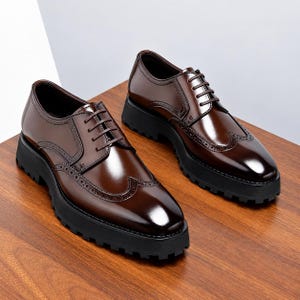 May include: A pair of dark brown leather wingtip oxford shoes featuring a polished finish, decorative brogue detailing, thin brown laces, and a thick, black, lugged rubber sole that provides a distinct contrast to the upper shoe design.