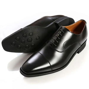 Könnte beinhalten: Ein Paar schwarze Lederschuhe mit Cap-Toe-Design. Die Schuhe haben einen Schnürverschluss und eine Gummisohle. Die Sohle eines Schuhs ist sichtbar und zeigt ein strukturiertes Muster.