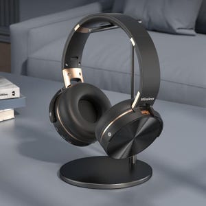 May include: Black wireless headphones with gold detailing rest on a black stand. The headphones feature a circular ear cup design and the word "Wireless" is printed on the side. The stand has a circular base.