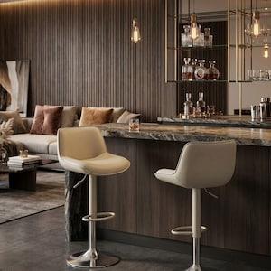 May include: Two cream-colored bar stools with curved backrests and padded seats. Each stool features a central silver-toned metal pedestal base, a circular footrest, and an adjustable height lever located beneath the seat cushion.