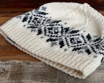 May include: White knitted hat with a black and gray geometric pattern. The hat is made of wool and has a folded brim.