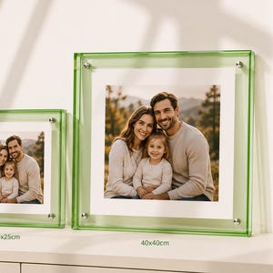 Peut inclure: Deux cadres photo carrés avec des bordures en acrylique vert clair translucide et des fixations argentées. Le plus petit cadre est marqué 25x25cm et le plus grand 40x40cm. Les deux cadres présentent une photographie d'une famille de trois personnes.