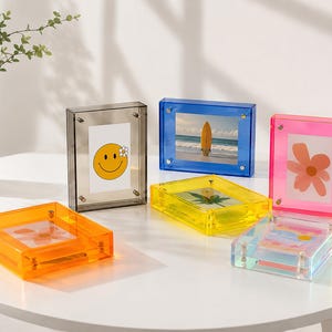 May include: A collection of six rectangular acrylic photo frames in vibrant translucent colours including orange, grey, blue, yellow, pink, and clear. Each frame features four silver-toned metal corner screws to hold the contents securely in place.