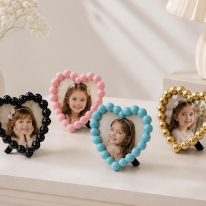 Peut inclure: Quatre cadres photo en forme de cœur avec un bord perlé. Les cadres sont disponibles en noir, rose clair, bleu clair et or métallique. Chaque cadre contient la photographie d'une jeune enfant et possède un petit support à l'arrière.