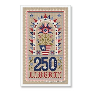 Op de afbeelding: Kruissteekontwerp met patriottische elementen. Een centraal bloemstuk in een vaas met een Amerikaans vlagontwerp wordt omlijst door een rode, witte en blauwe boog. Het nummer "250" en het woord "LIBERTY" zijn eronder geborduurd. Het ontwerp is omlijst in een witte rand.