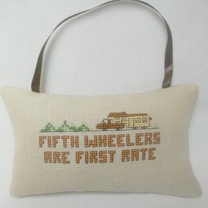 May include: A beige fabric pillow with a brown ribbon loop for hanging. The pillow has a cross-stitch design of a fifth wheel camper and the text "FIFTH WHEELERS ARE FIRST RATE".