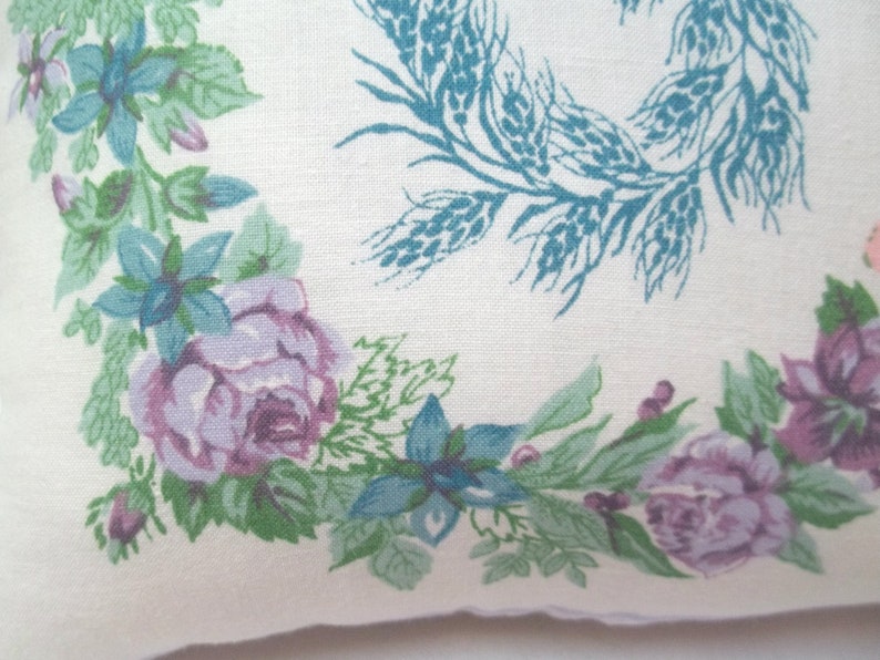 Puede incluir: Una tela blanca con un patr&oacute;n floral que presenta flores azules y moradas, hojas verdes y espigas de trigo. La tela tiene una est&eacute;tica vintage.