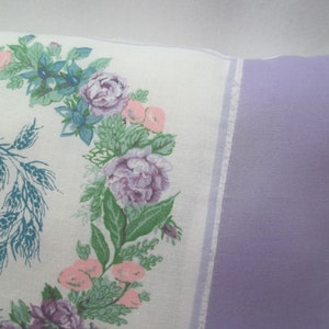 Puede incluir: Una almohada blanca con un dise&ntilde;o floral que presenta una corona de trigo y flores rosas, moradas y azules. La almohada tiene un respaldo de color lavanda.