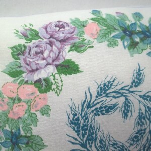 Puede incluir: Una funda de almohada blanca con un dise&ntilde;o floral que presenta rosas rosas y moradas, hojas verdes y flores azules. El dise&ntilde;o tambi&eacute;n incluye una corona de espigas de trigo en color azul verdoso.