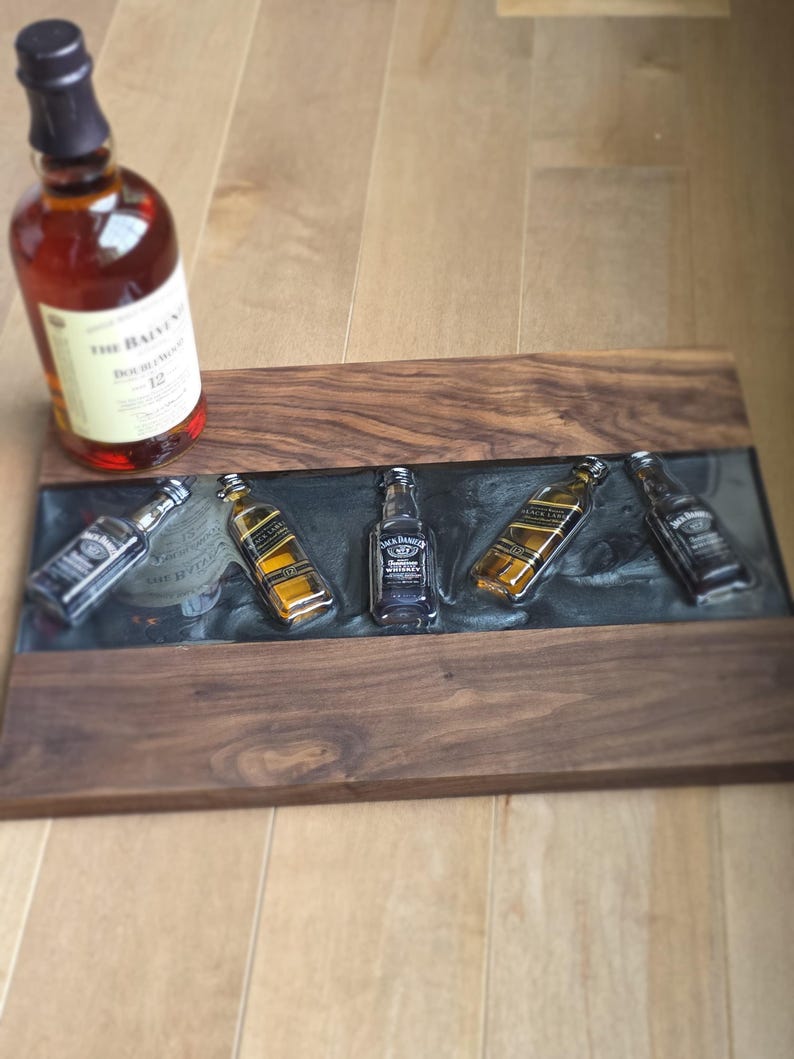 Pode incluir: Uma bandeja de madeira com uma incrusta&ccedil;&atilde;o de resina ep&oacute;xi escura, com garrafas de whisky em miniatura. Uma garrafa de The Balvenie Doublewood 12 est&aacute; &agrave; esquerda. A bandeja &eacute; feita de madeira escura.