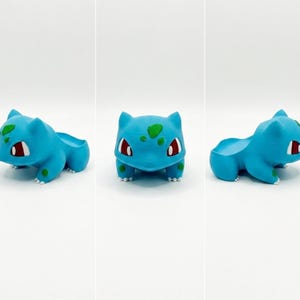 May include: A light blue Bulbasaur planter with green spots and red eyes. The planter is in the shape of the Pok&eacute;mon character, with a small opening on its back for plants. The planter is 3D printed.